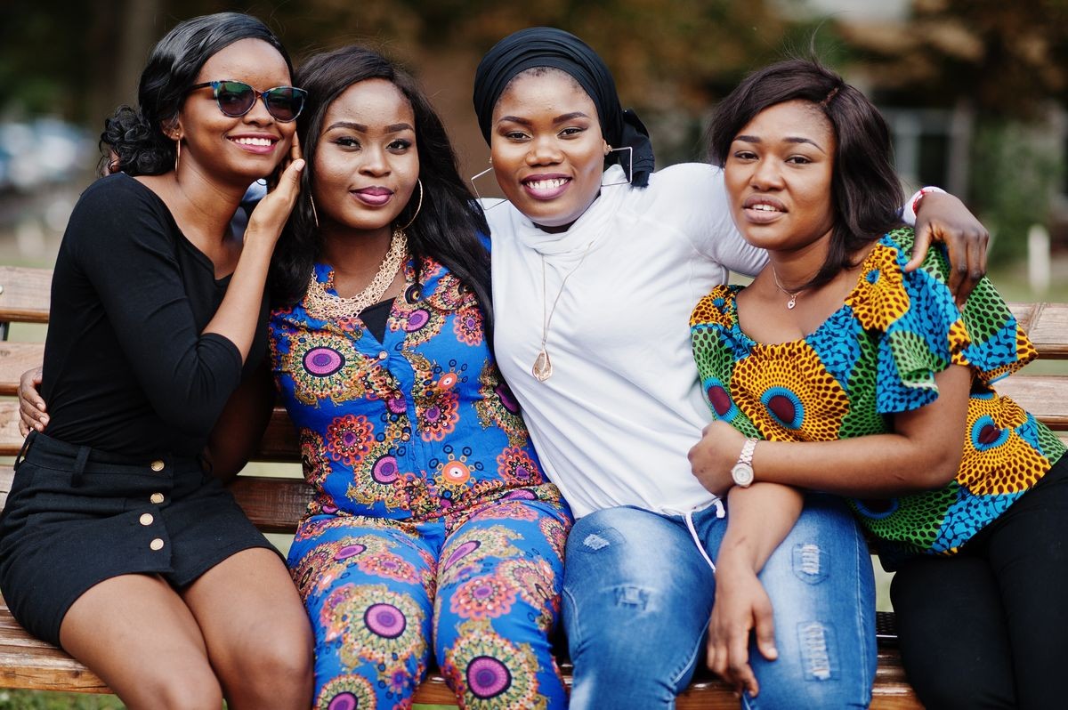 Group of four african american girls sitting on bench outdoor and hugs.