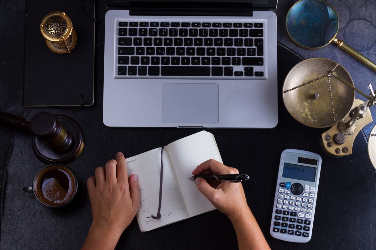 Workspace hero header with law gavel, legal book and laptop keyboard, open empty notebook with someones hands writting in notebook, top view flat lay scene